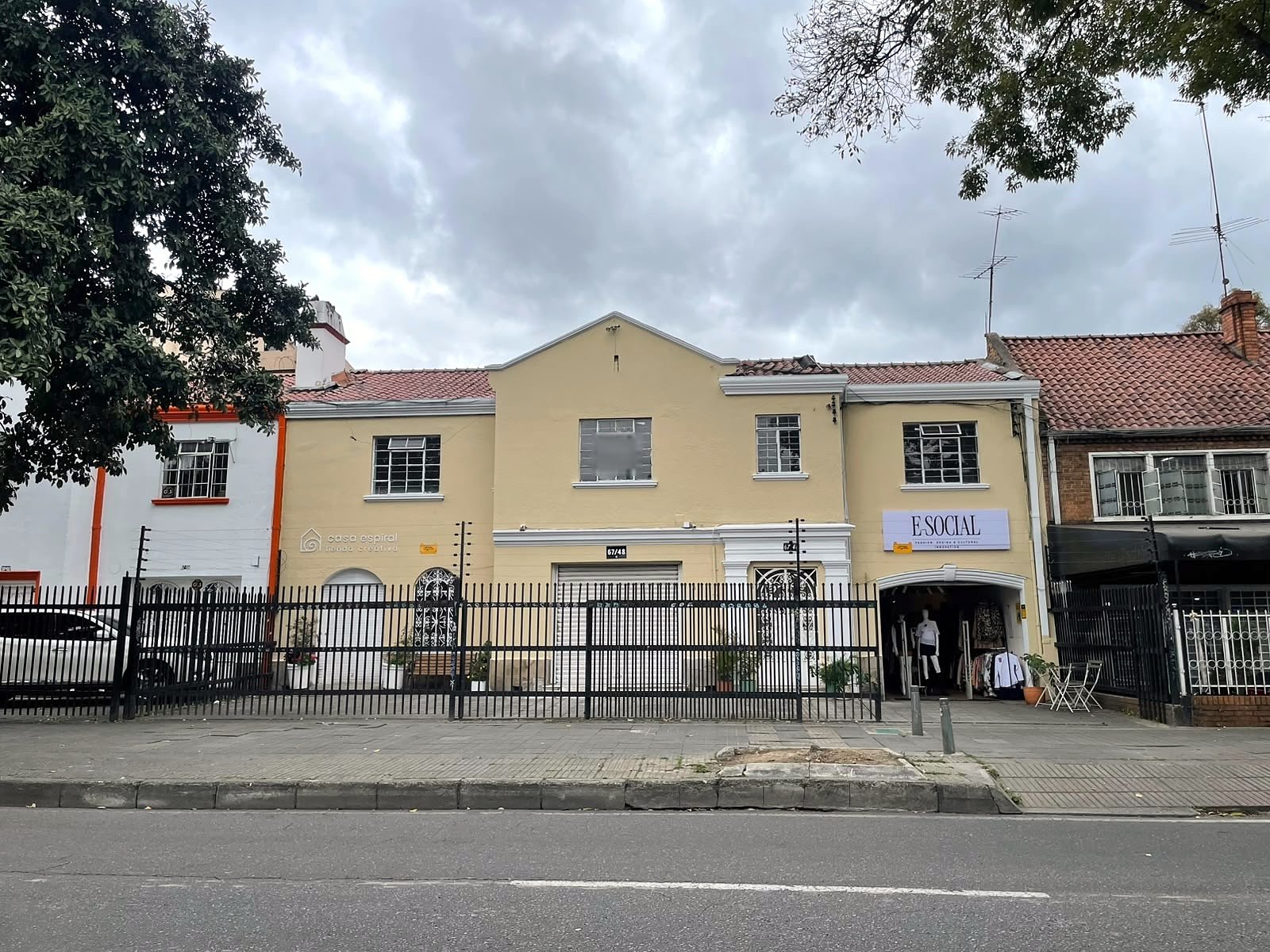 Street facade of the building on Carrera 11: yellow stucco, clay-tile roof, arched shopfront bay and wrought-iron fence